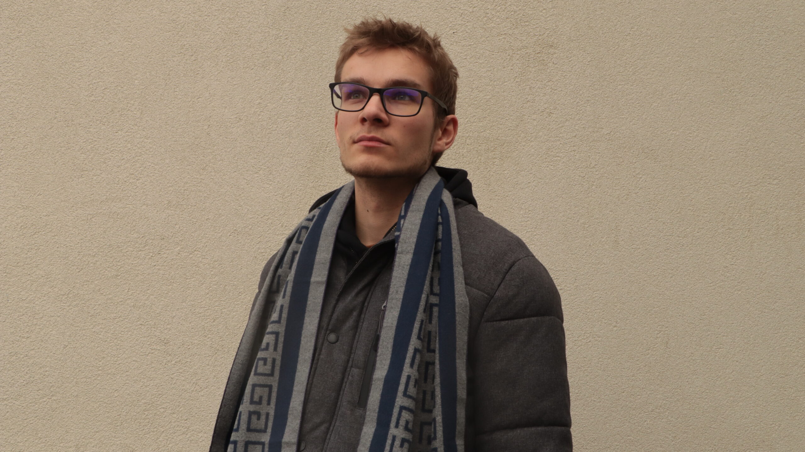Corentin GEORGES avec manteau gris foncé et écharpe bleu regardant, pensif, vers le haut